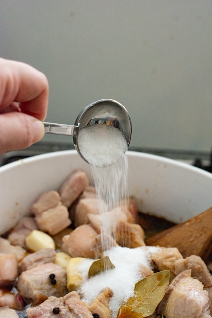 pouring sugar over pork belly adobo