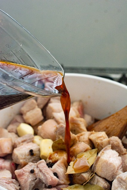 pouring sauce over pork belly for pork belly adobo