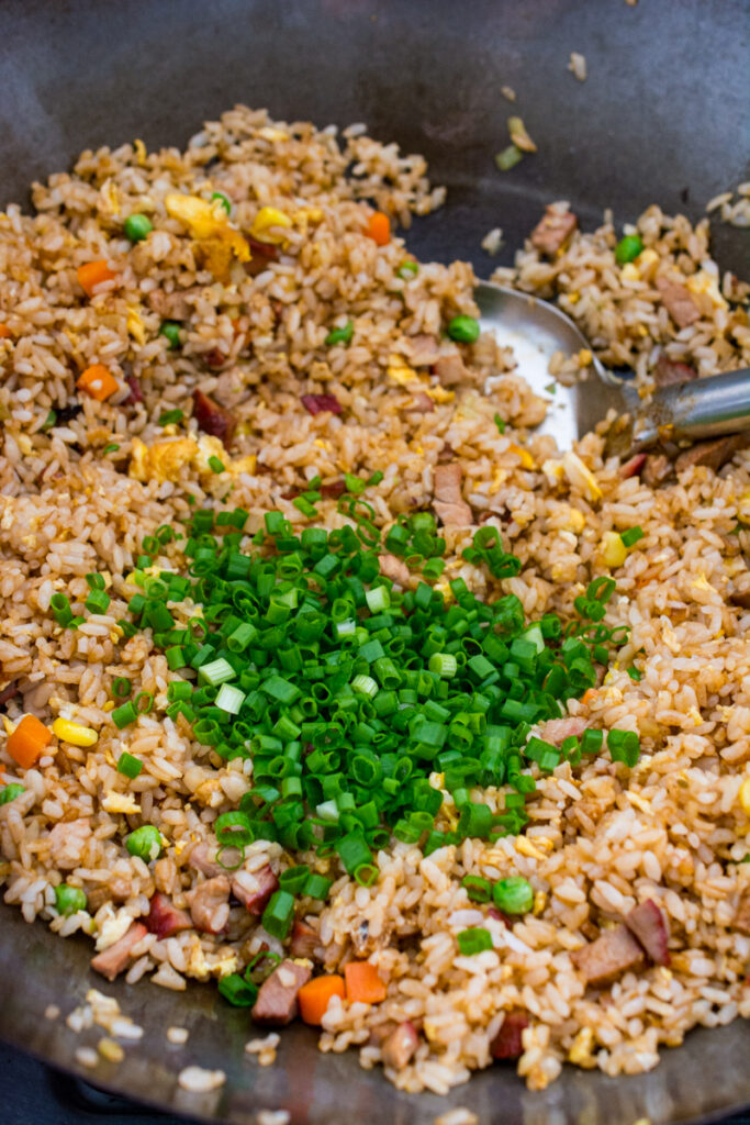 chinese bbq pork fried rice with chopped scallions in a wok