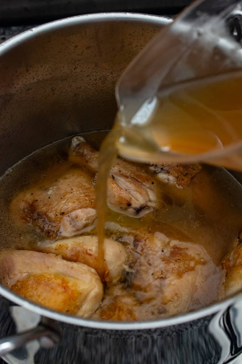 pouring chicken stock over pan-fried chicken thighs and drumsticks